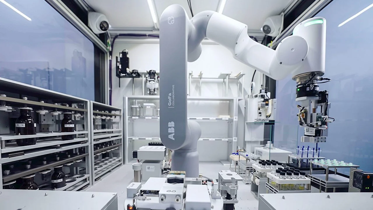 A robotic arm in a laboratory workspace surrounded by shelves with small bottles and various scientific equipment.