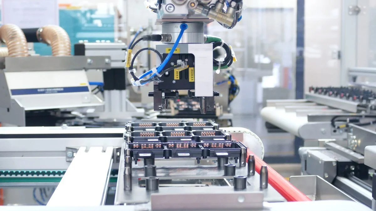 Close-up of an automated manufacturing assembly line with robotic arm and conveyor system processing electronic components.