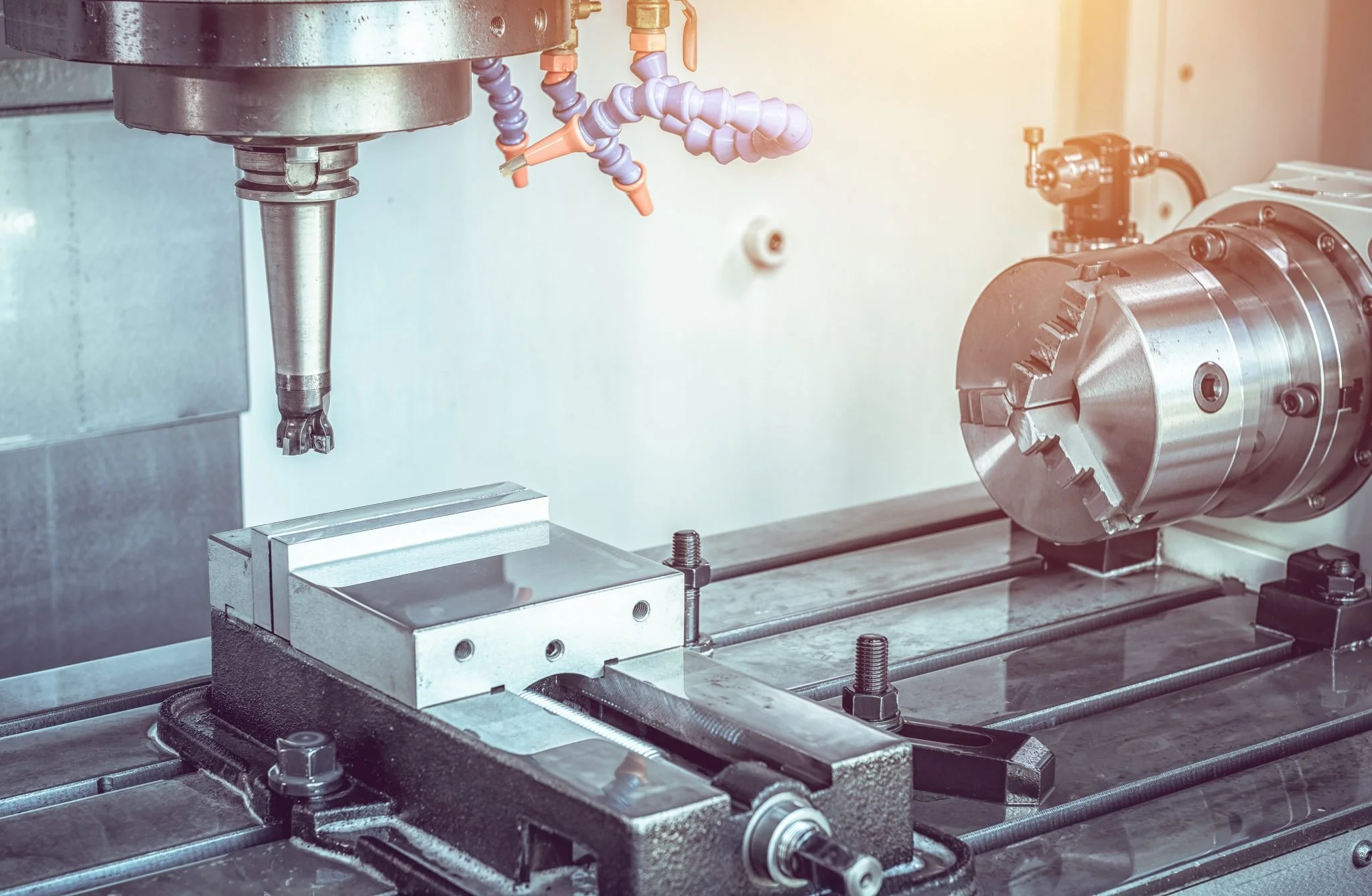 Close-up of a CNC machine with a drill bit, metal workpiece, and rotary tool in an industrial setting.
