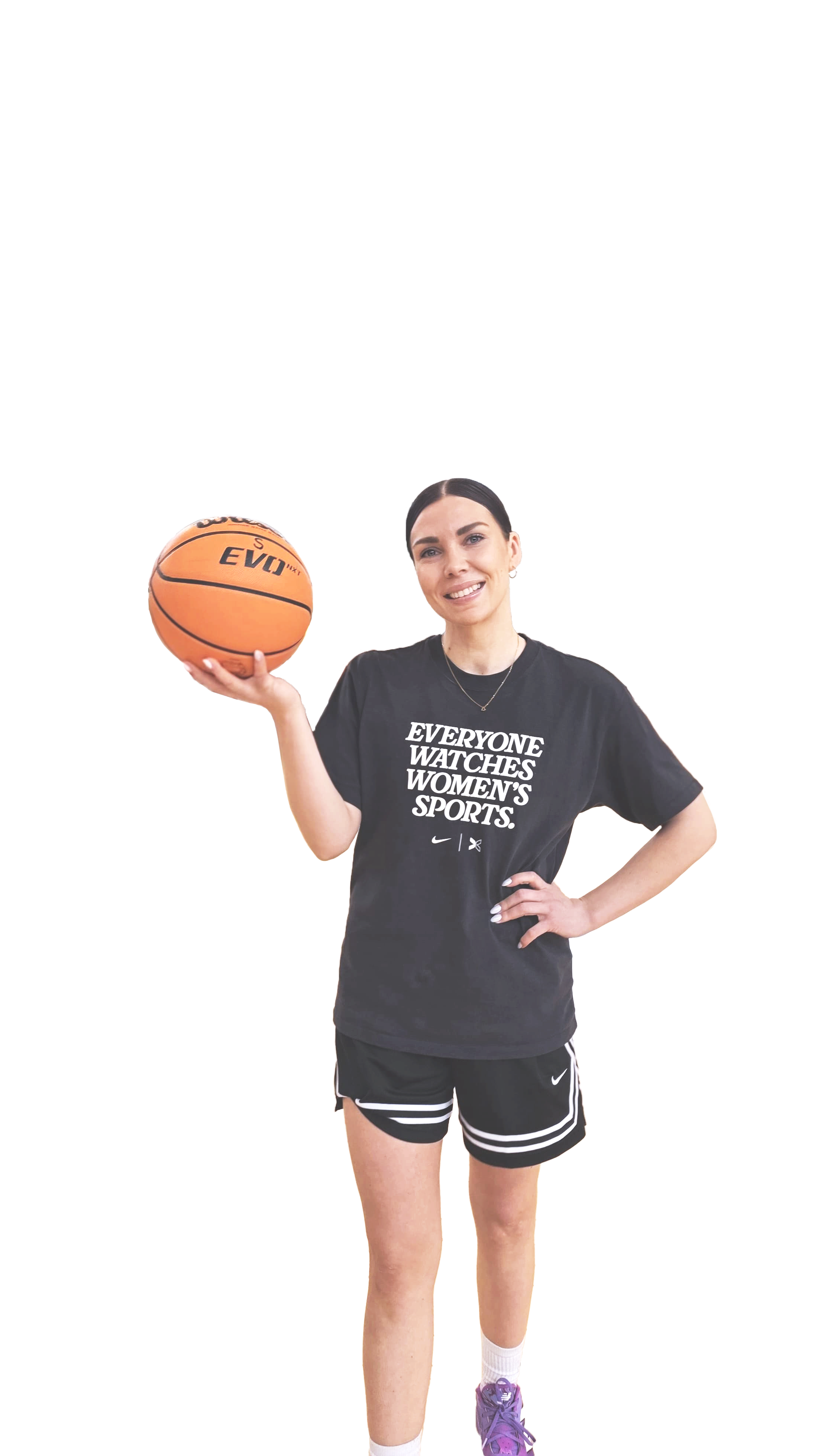 Nuori nainen, joka pitää koripalloa oikeassa kädessään, hymyilee ja katsoo kameraan. Hänellä on musta T-paita, jossa lukee 'EVERYONE WATCHES WOMEN'S SPORTS.', sekä mustat urheilushortsit ja lenkkarit.