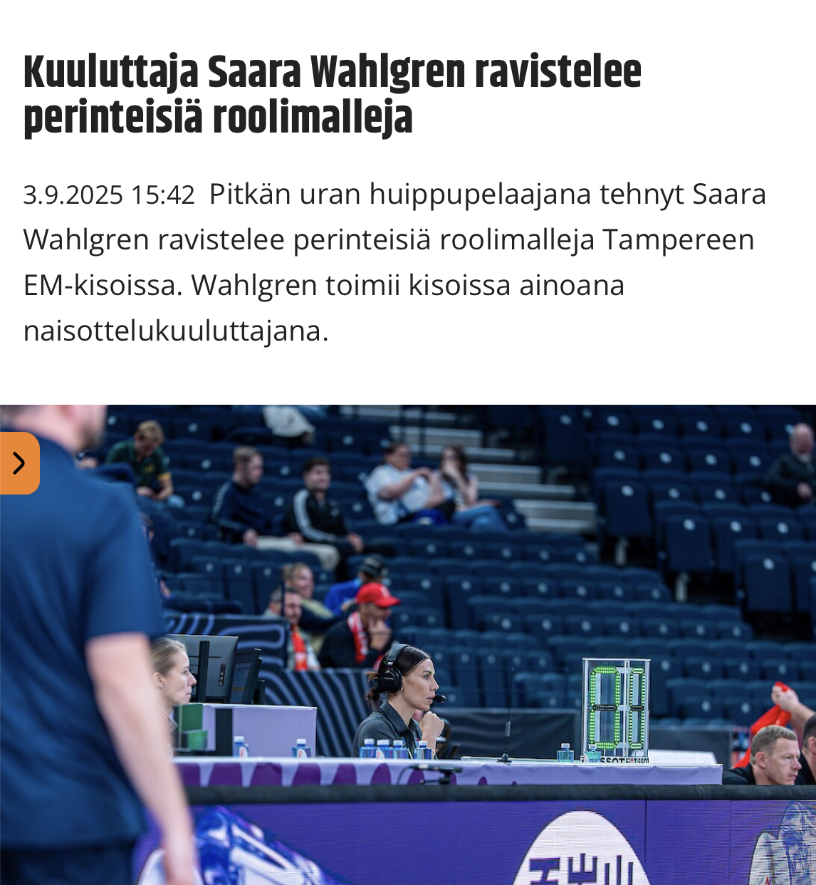 Kuva urheilutapahtumasta koripallo-ottelusta, jossa pelikentän laidalla digitalinäyttö ja henkilöitä istumassa katsomossa.