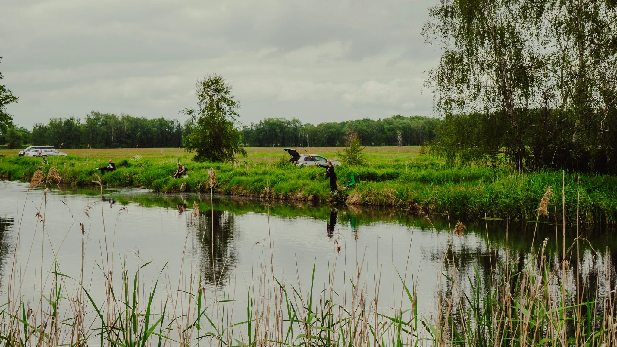 Menschen beim Angeln an einem Fluss in einer grünen, bewölkten Landschaft