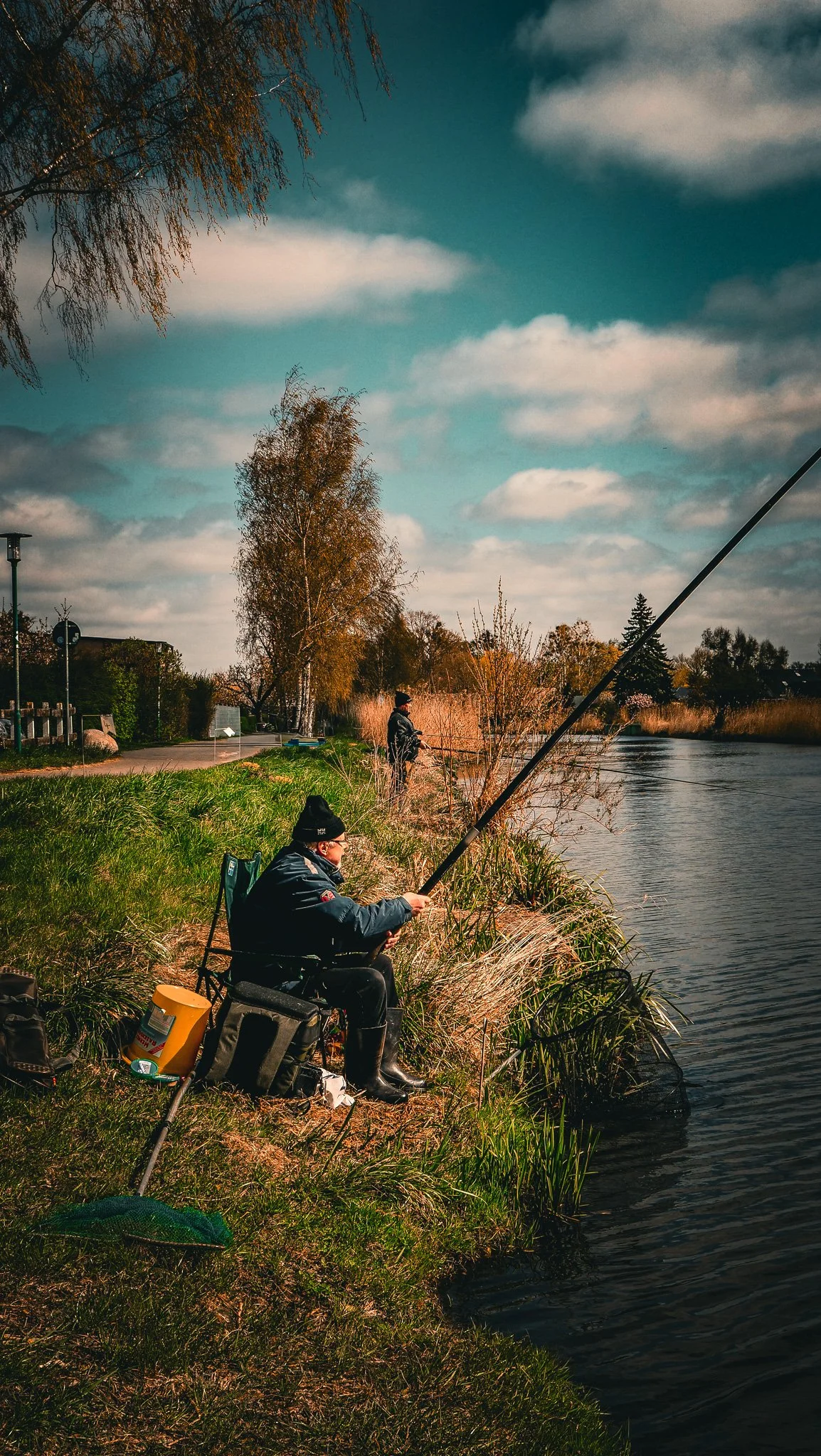 Fischer sitzen entspannt am Flussufer, fangen Fische und genießen die Natur bei bewölktem Himmel im Herbst.