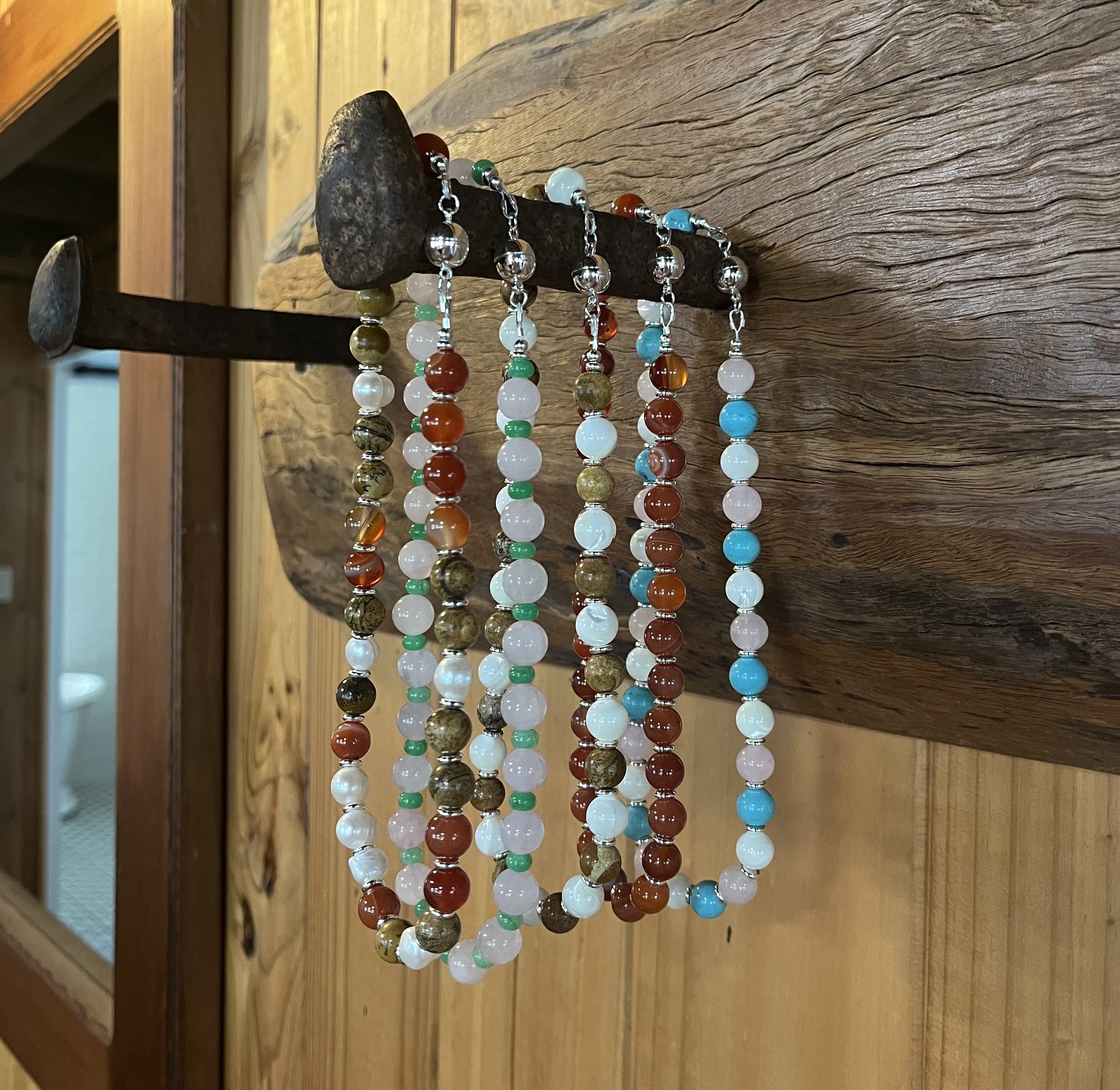 Colorful beaded necklaces hanging on a rustic wooden rack.