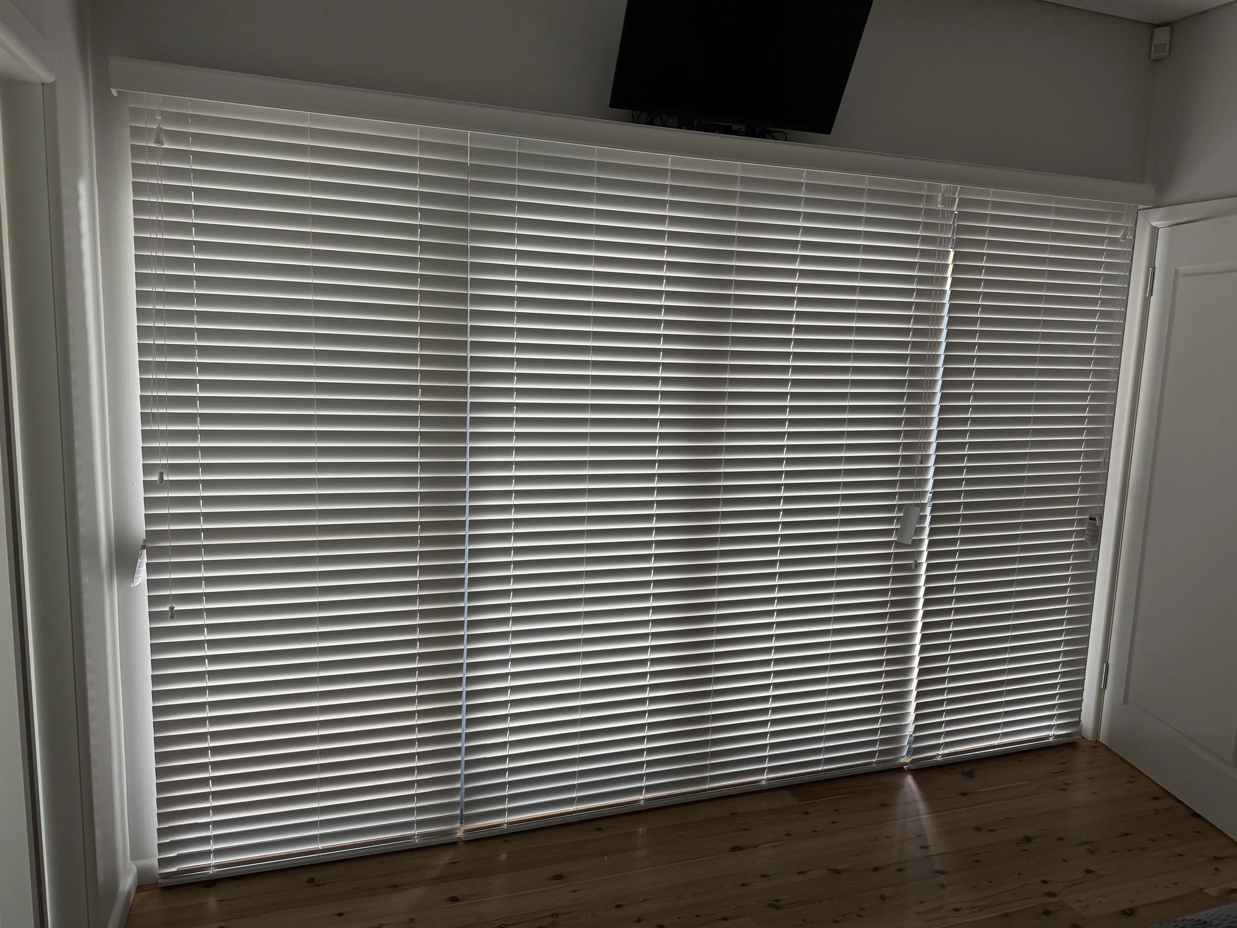 White PVC Venetian blinds adjusted for increased privacy and glare control in a living room.