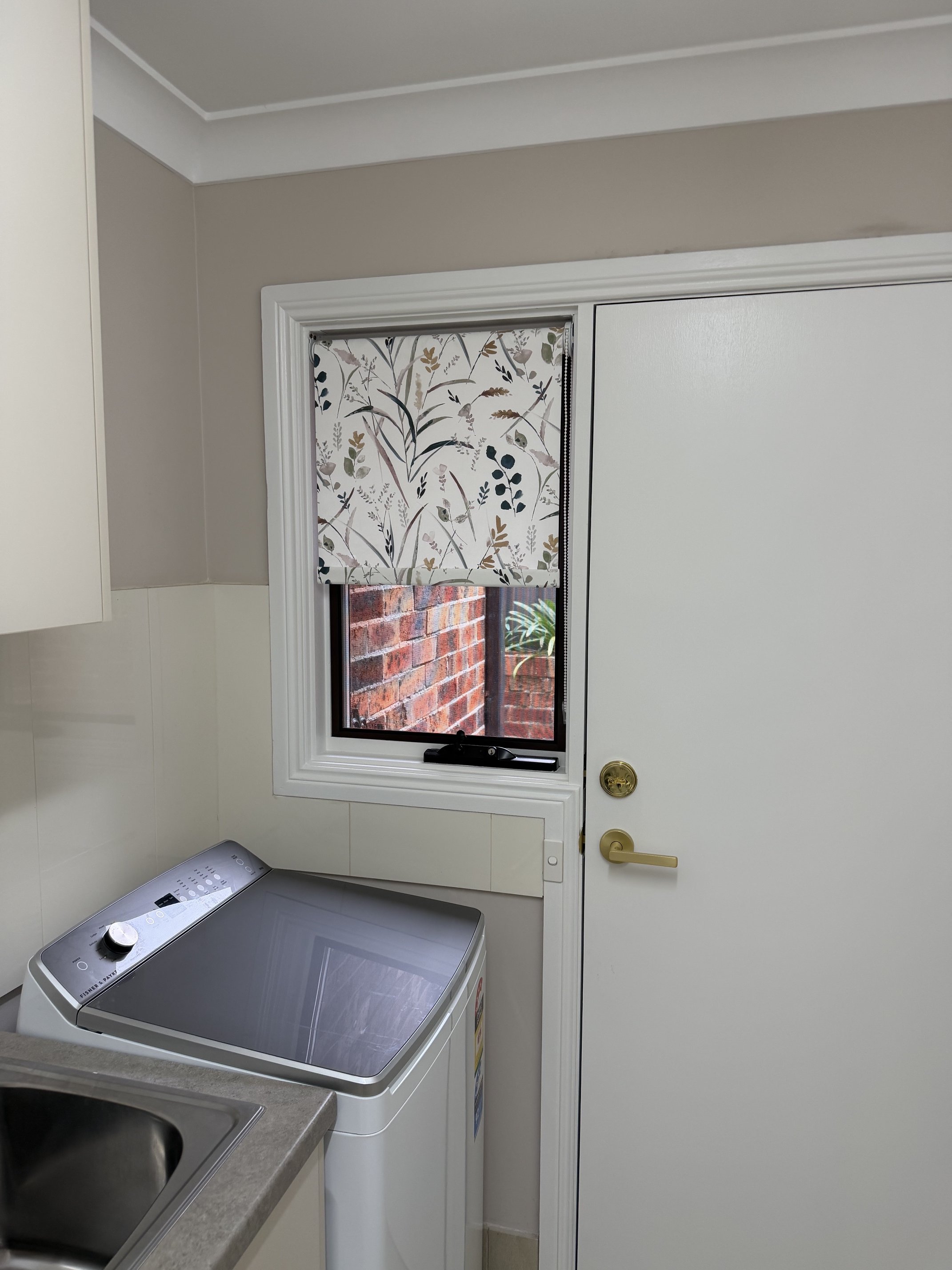 Pattern fabric roller blind partially lowered in laundry room