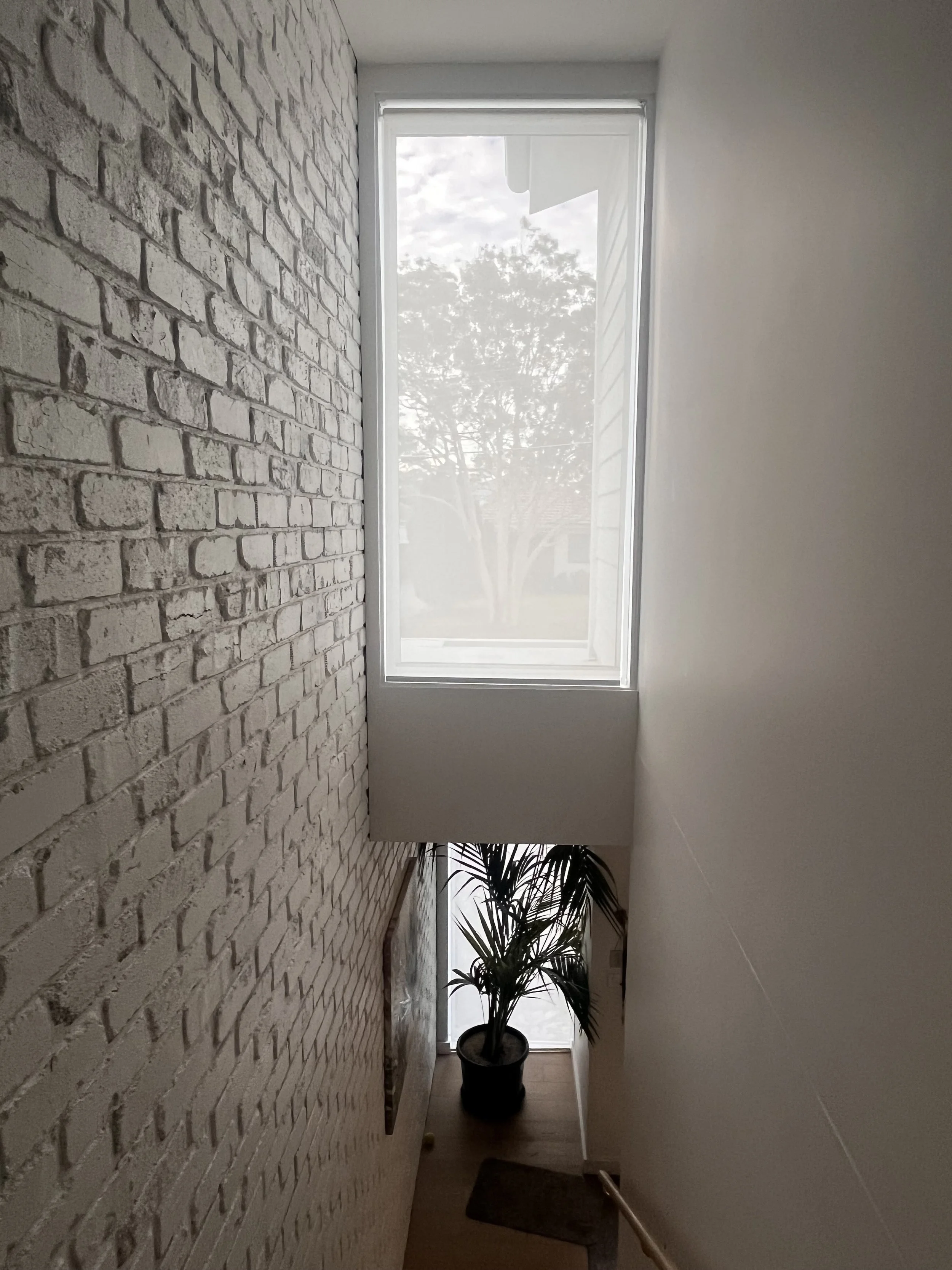 Roller blind installed over a staircase window providing privacy while maintaining natural light.
