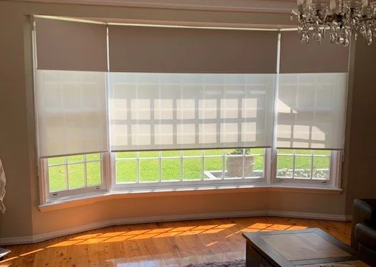 Double roller blinds with sheer and blockout fabric in a bay window living room, allowing soft natural light through.