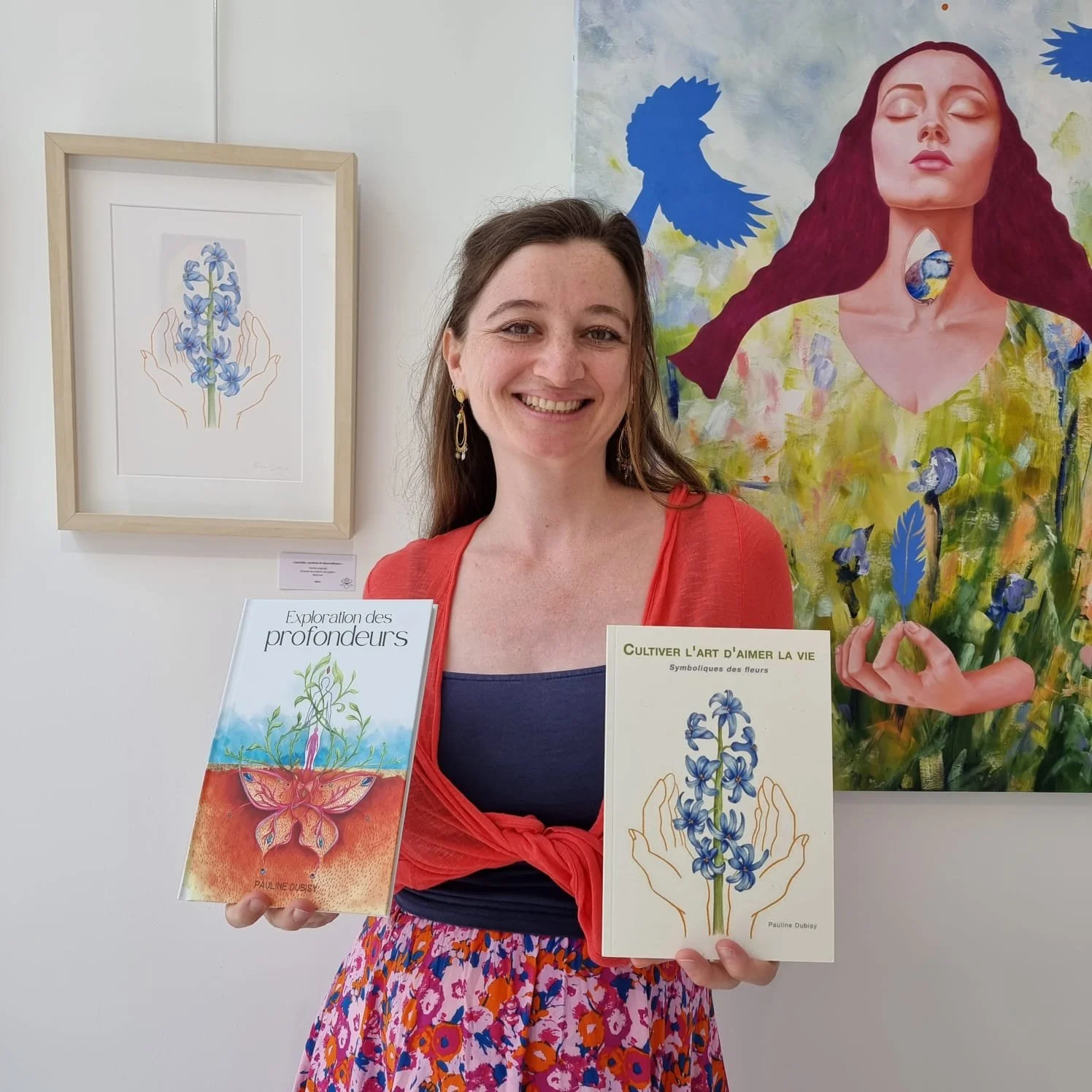 Une femme souriante tient deux livres, l'un intitulé « Exploration des profondeurs » avec une illustration de fleurs et un insecte, l'autre intitulé « Cultiver l'art d'aimer la vie » avec une illustration de fleurs dans les mains. Elle se tient devant une œuvre d'art représentant une femme avec une colombe sur la tête, en arrière-plan.