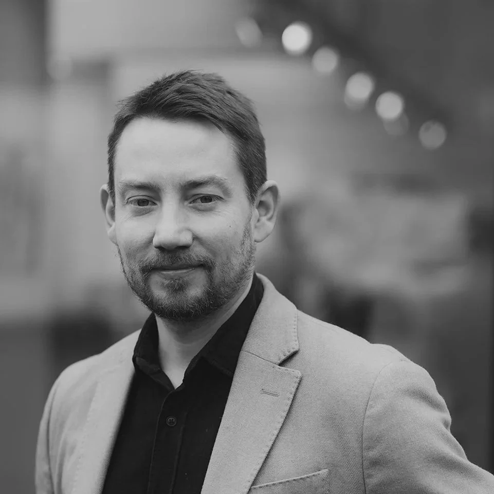 Portrait d'un homme d'affaires en costume, souriant, avec un fond flou.
