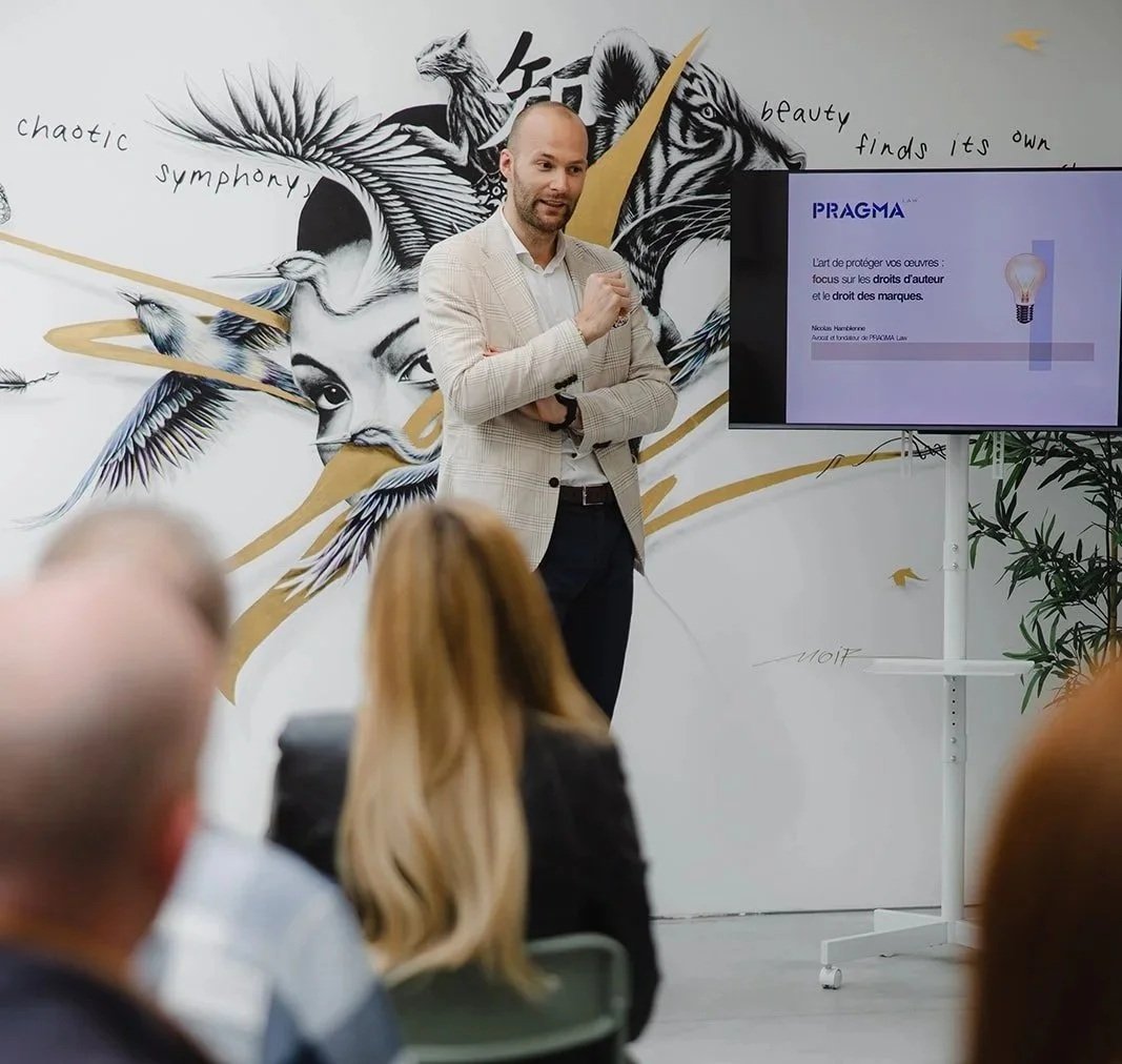 Un homme en costume donne une présentation devant un tableau avec une illustration artistique de visages de femmes, d'oiseaux et d'animaux, avec une montre dorée en ligne de temps. Un écran affiche une diapositive intitulée "PRAGMA".