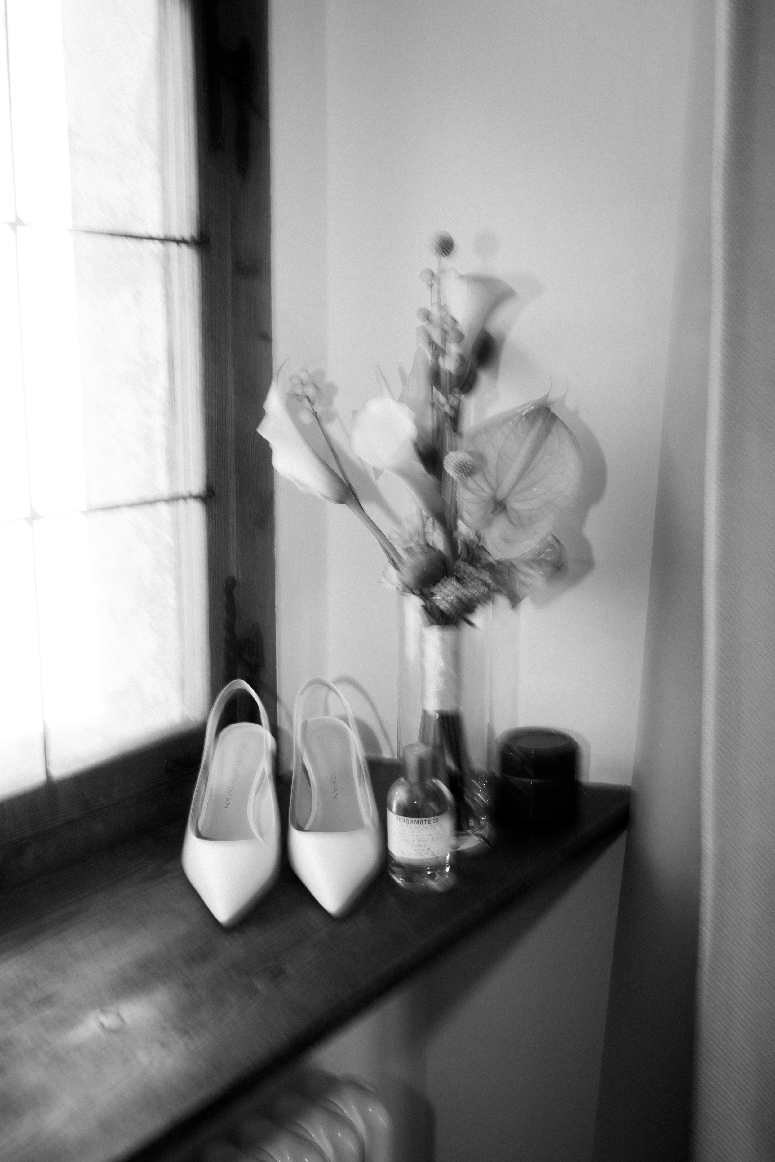 Blumen in einer Vase, eine Wasserflasche auf einem Tisch, vier weiße Steh-Lampen, ein schwarzer Lautsprecher, ein dunkles Fenster in einem Raum.