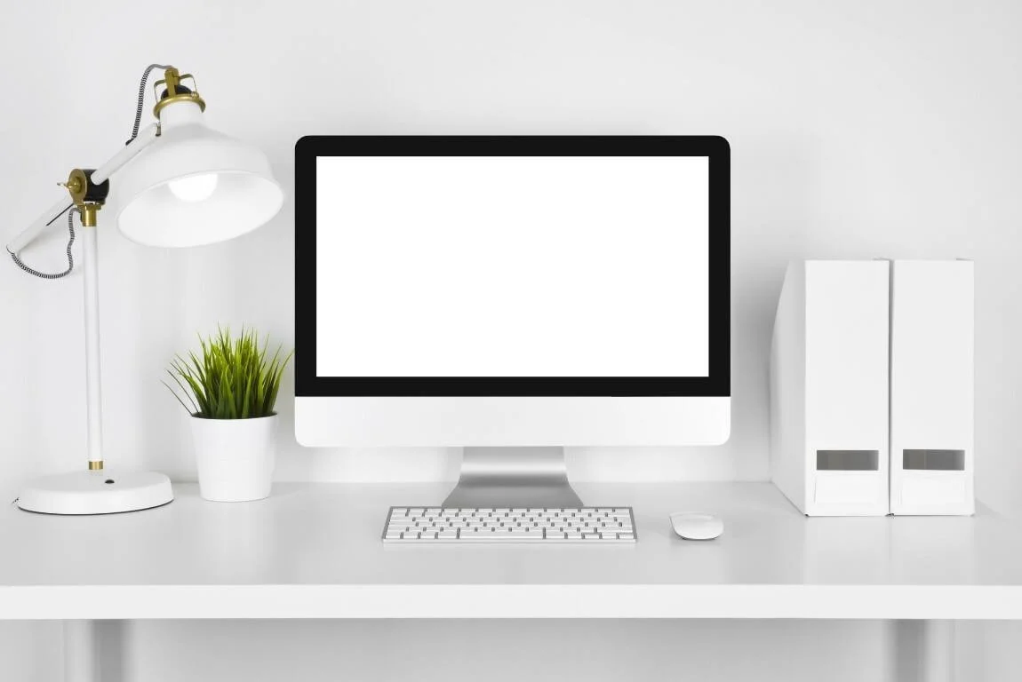 Bureau minimaliste avec une lampe de bureau, un pot de plantes vertes, un ordinateur, un clavier, une souris et deux classeurs blancs
