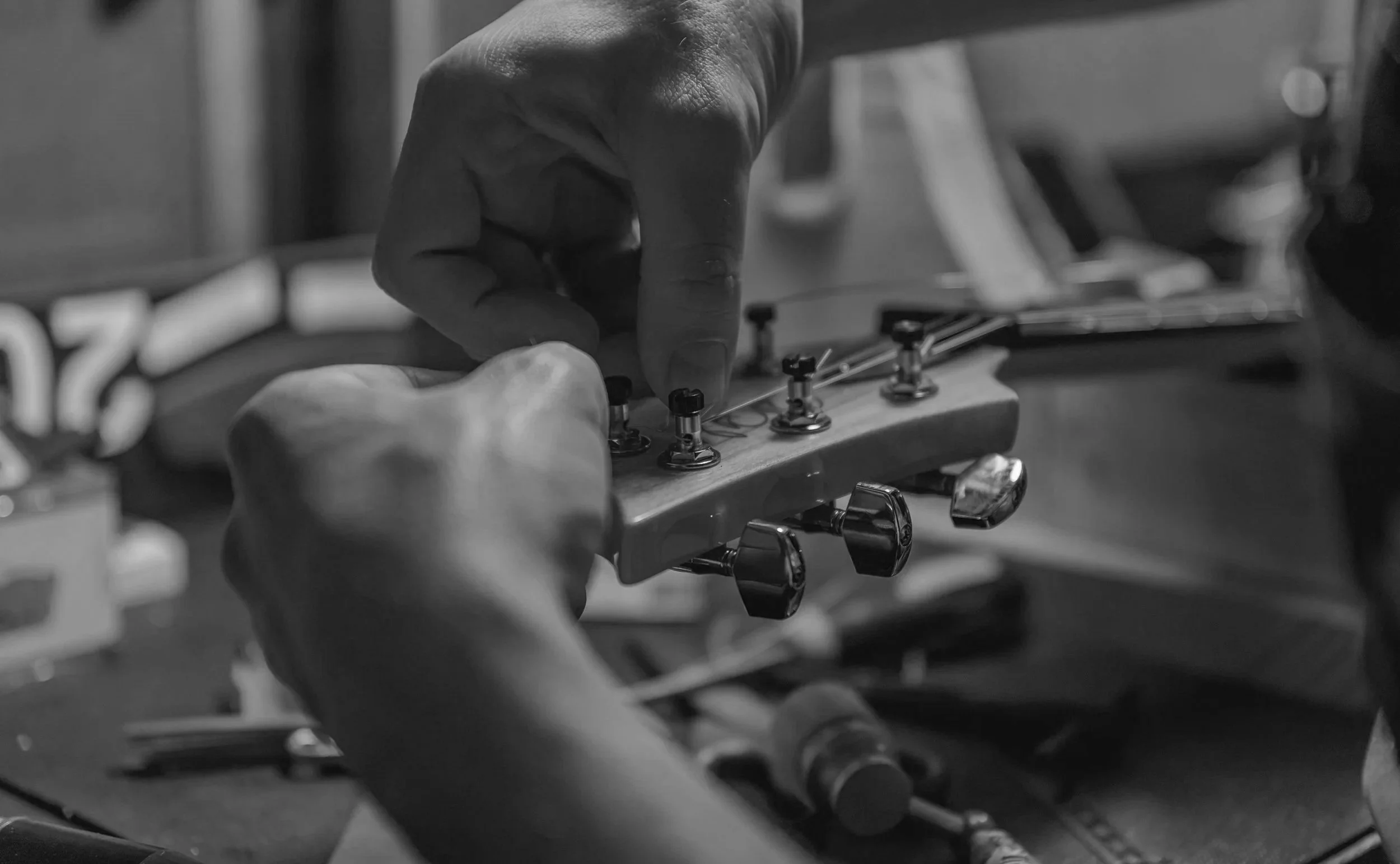 Close-up of a person's hand tuning a guitar's headstock with tuning pegs, in black and white.