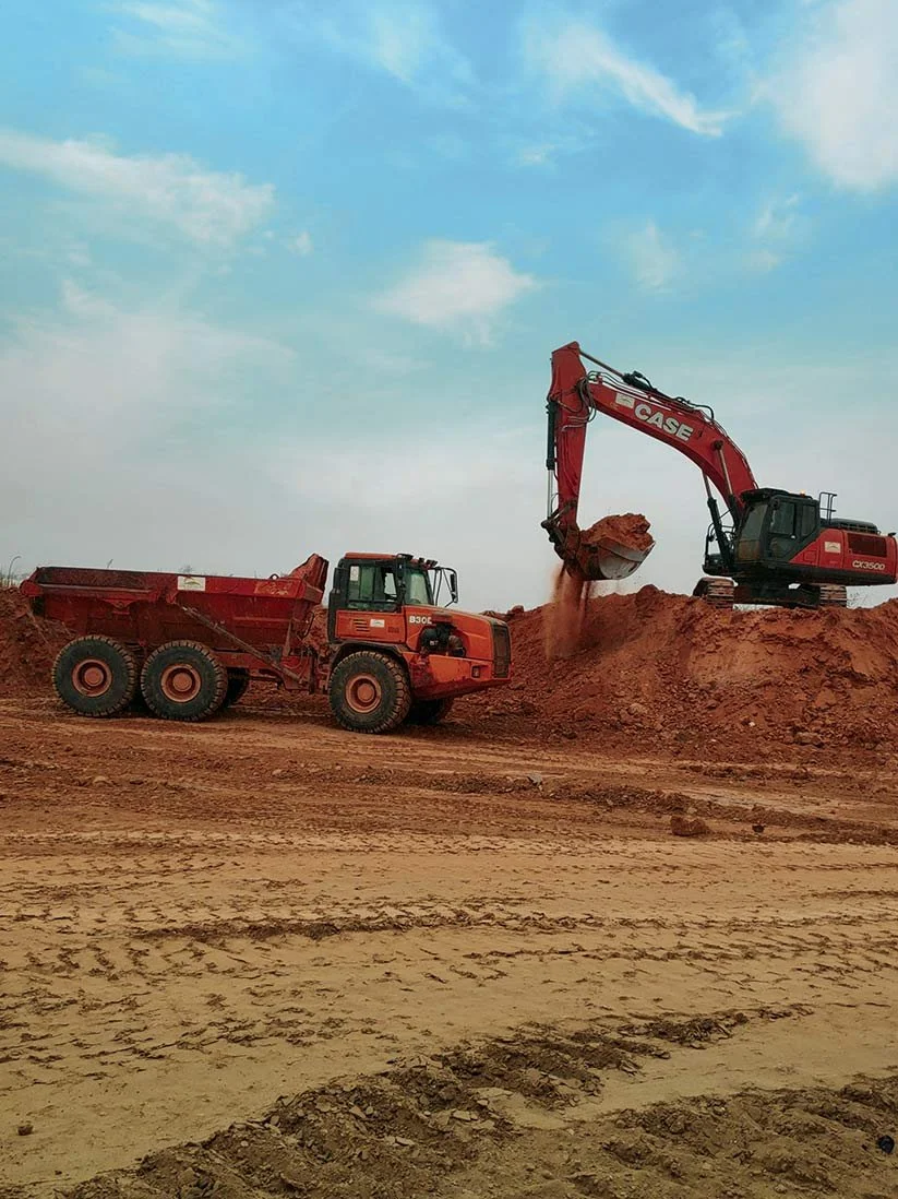 Caminhão e escavadeira operando na construção civil em um canteiro de obras ao ar livre.