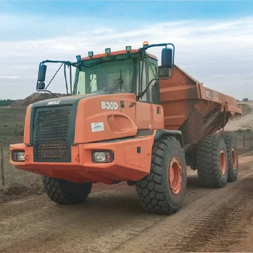 Caminhão de carga de cor laranja em um terreno de terra, ao fundo céu nublado.