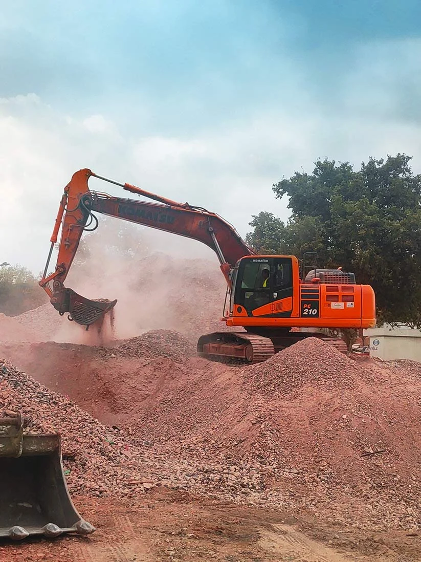 Escavadeira realizando escavação em uma área de terra com árvores ao fundo.