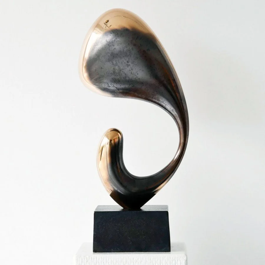 Abstract sculpture with a curved, swirling shape in metallic bronze and black, mounted on a black rectangular base