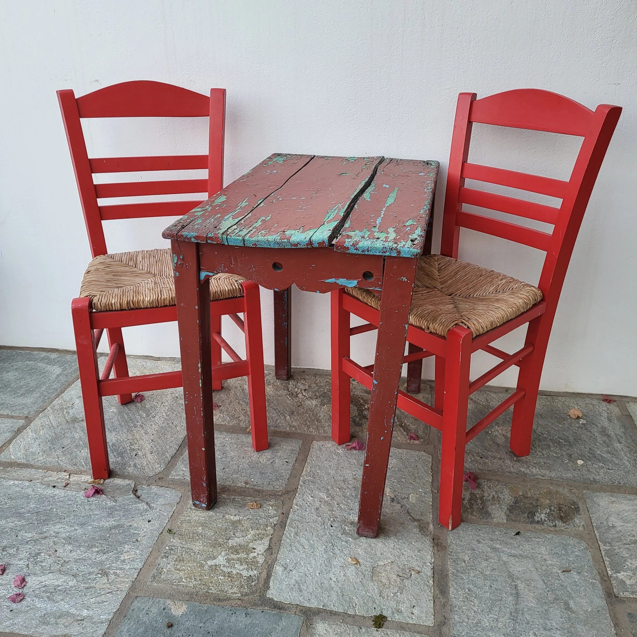 Chaises rouges avec assises en corde de paille autour d'une petite table en bois peint délavé et usé.