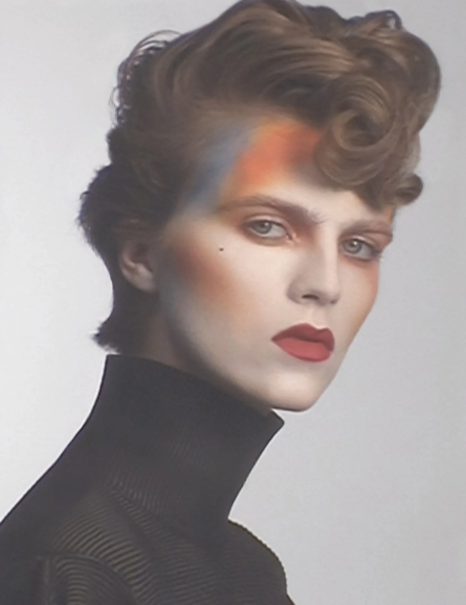 Close-up of a woman's face and upper body with styled short brown hair, light eye makeup, red lipstick, wearing a black turtleneck, against a gray background.