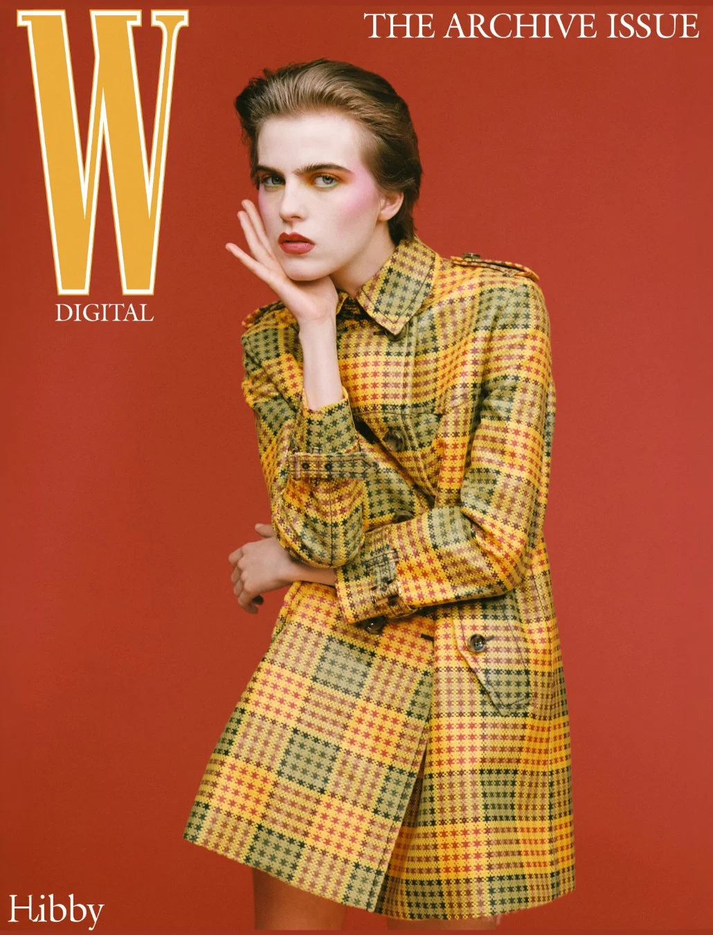 Cover of W magazine's archive issue featuring a woman with short brown hair in a yellow and green plaid coat, posing with her hand near her face against a red background.