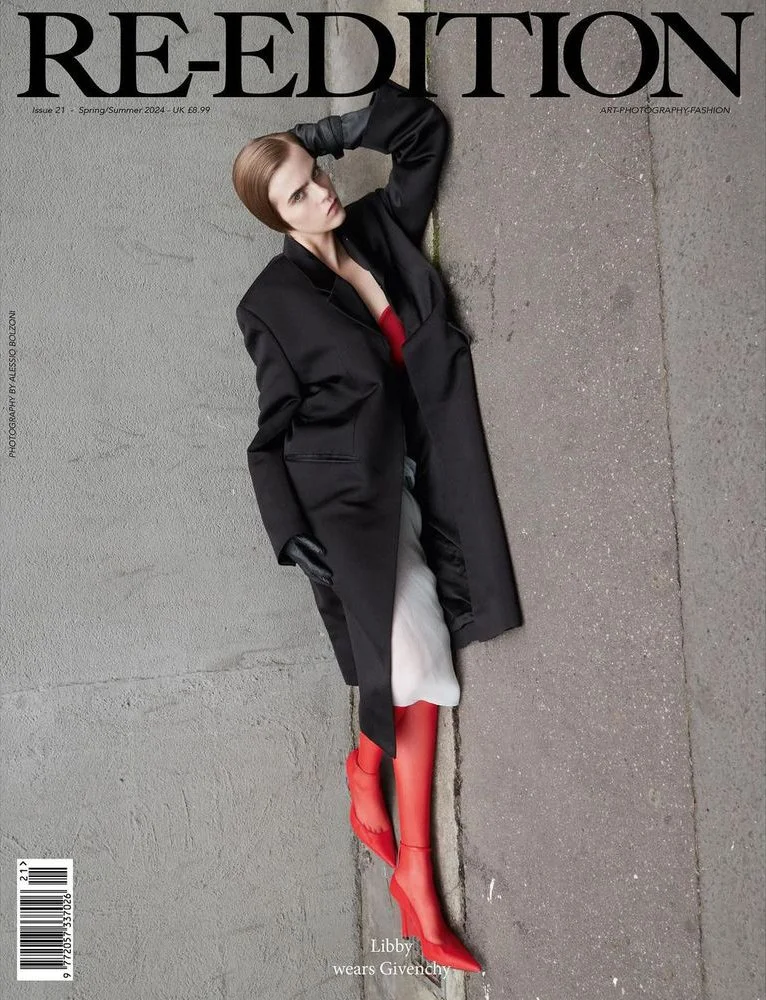 A woman with short brown hair is lying on a sidewalk, wearing a black coat, red top, light gray pants, red socks, and red shoes. She is posing with one arm resting on her head. The cover features the title 'RE-EDITION' and the subtitle 'Libby wears G