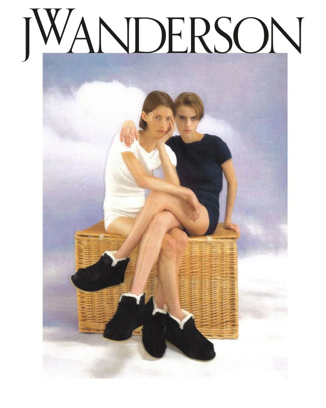 Movie poster for "J WanderSon" featuring two young women sitting on a wicker trunk, with a clouds background. One woman has brown hair and is wearing a white dress, the other has blonde hair and is wearing a navy dress.