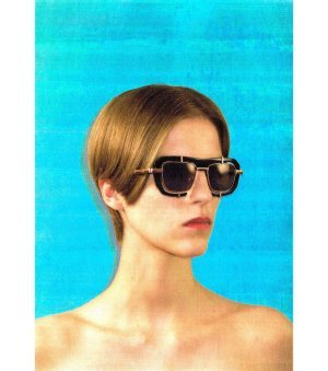 Woman with short hair wearing oversized black sunglasses against a blue background.