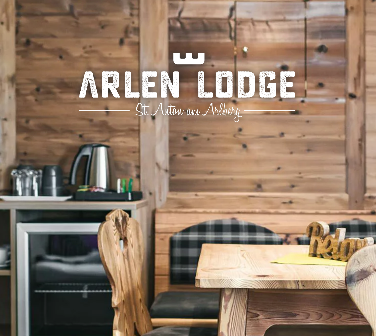 Inneneinrichtung eines Holzlodges mit einem Holz-Esstisch, Stühlen und einem kleinen Kühlschrank, im Hintergrund eine Holzverkleidung an den Wänden.