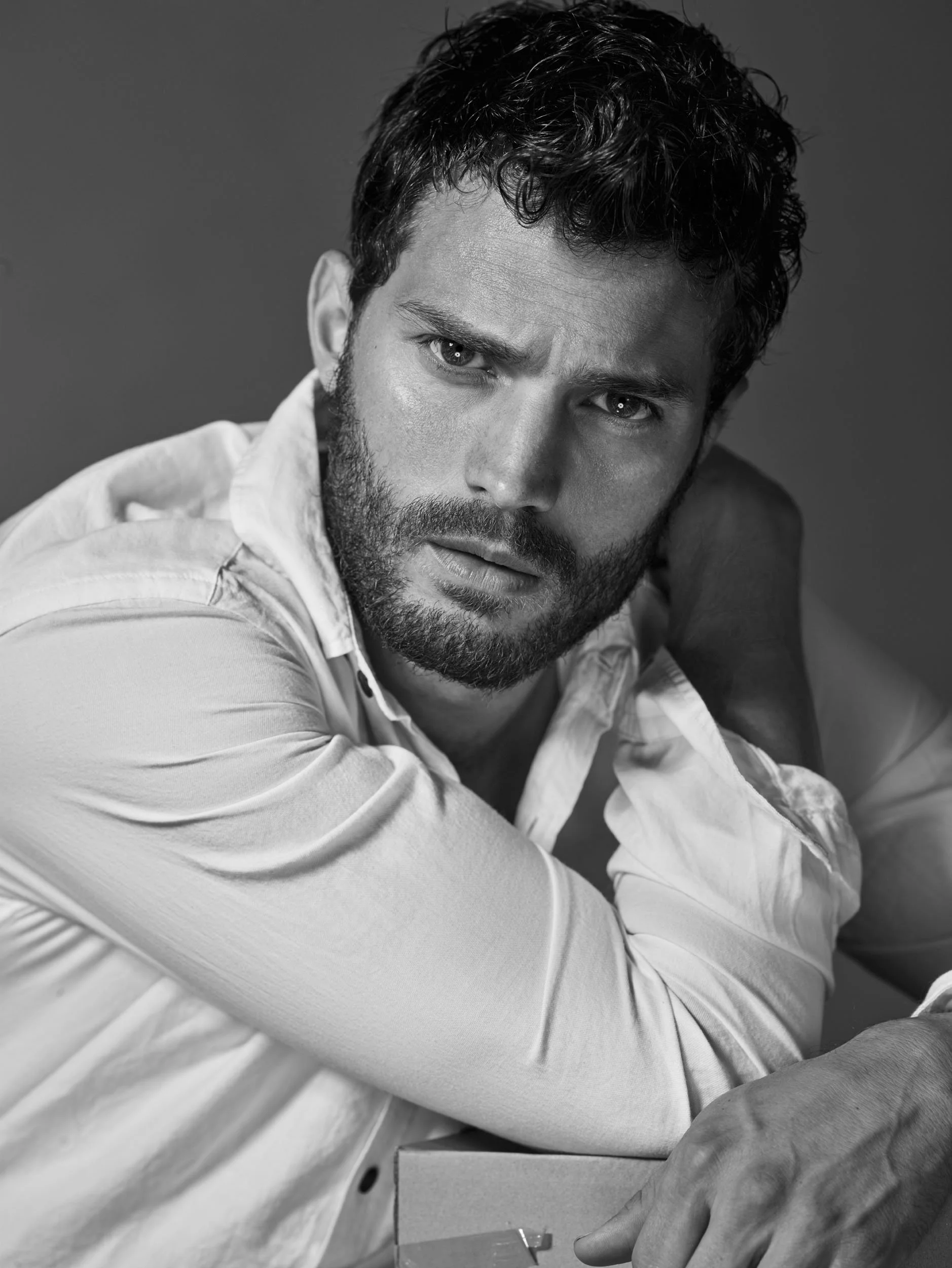 Black and white photo of a man with a beard and curly hair, wearing a light-colored shirt, looking directly at the camera with a serious expression.