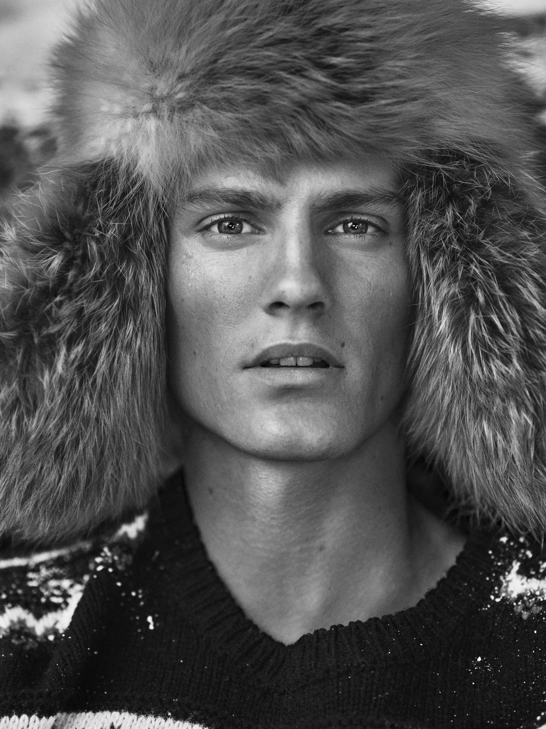 Black and white portrait of a woman wearing a fur-lined hooded coat, with a neutral expression, directly facing the camera.