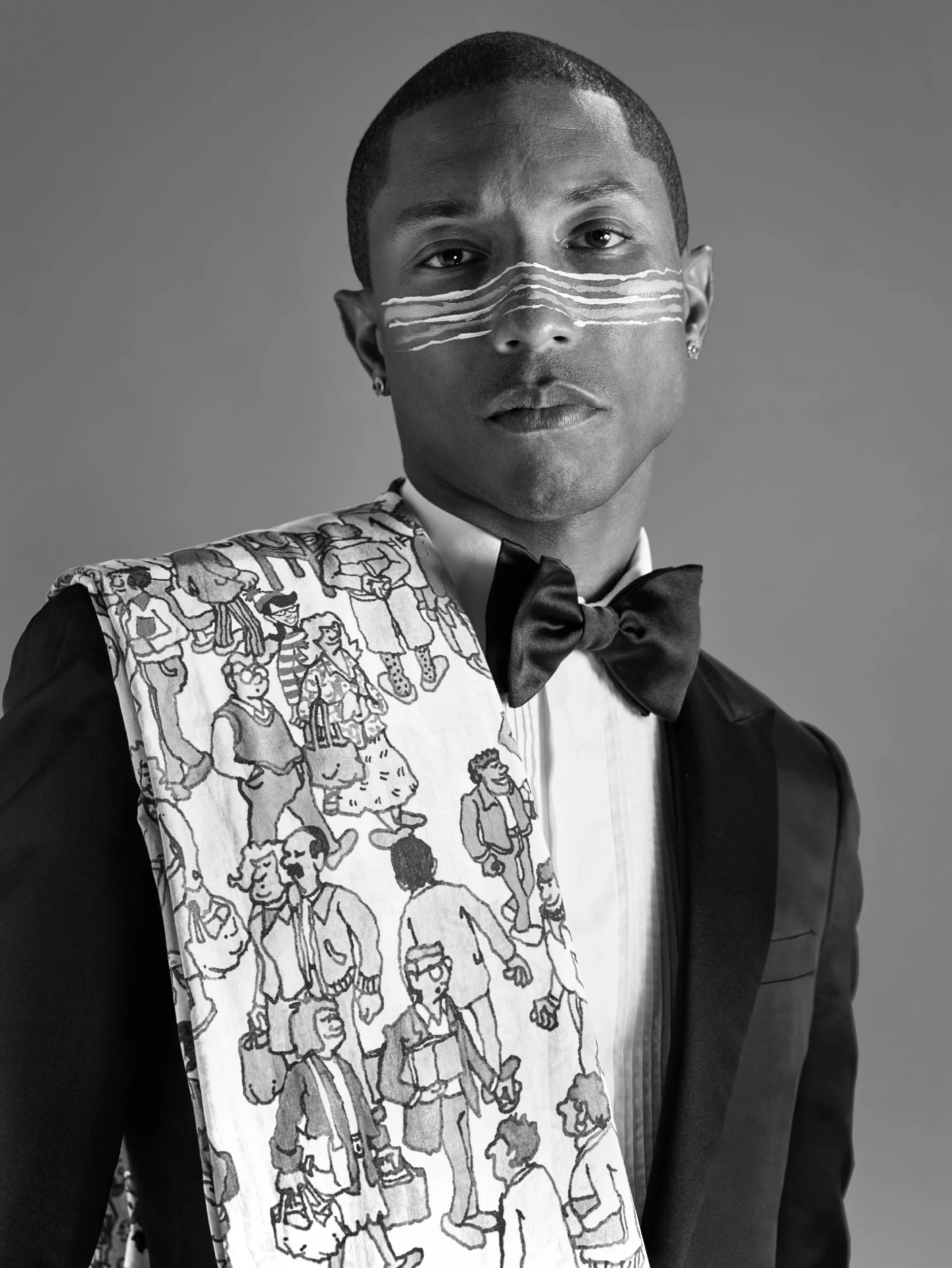 Black and white portrait of a person in formal attire, wearing a tuxedo with a bow tie and a patterned scarf over their shoulder. The person's face has three white lines painted across the nose, and they have short hair and earrings, against a plain 