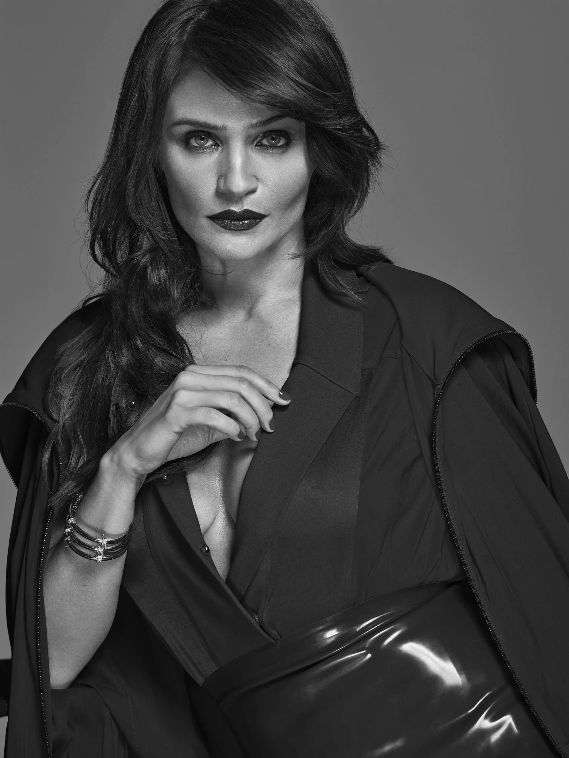Black and white portrait of a woman with long, styled hair, wearing dark lipstick and a fashionable outfit, looking directly at the camera.