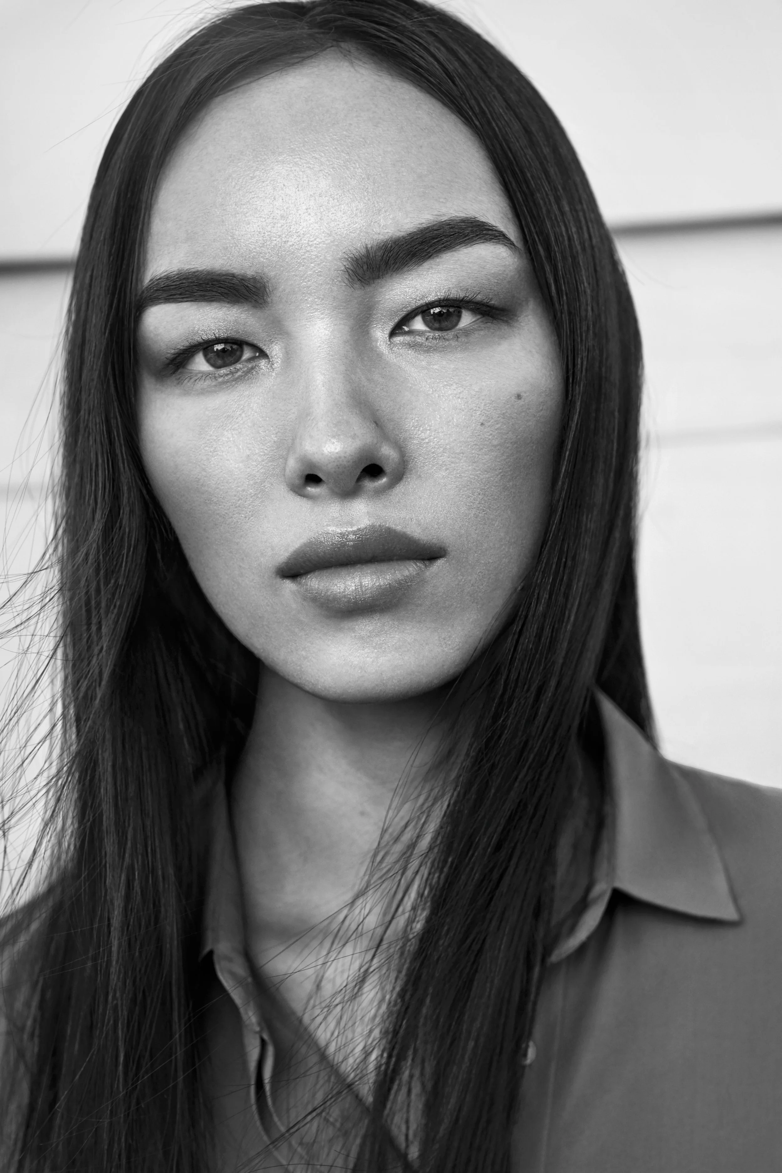 Black and white portrait of a woman with long, straight hair, wearing a collared shirt, looking directly at the camera with a serious expression.