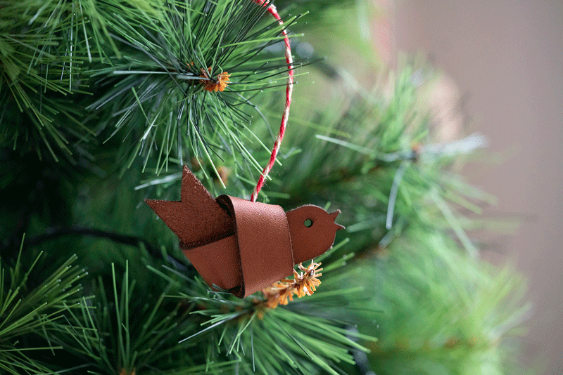 Lasergeschnittener Vogel aus Leder als Weihnachtsbaumschmuck an einem Tannenzweig
