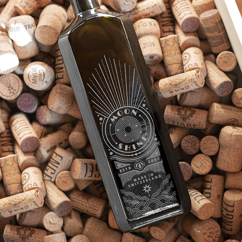 Dunkle Flasche mit lasergraviertem Moonshine Design, liegend auf Weinkorken