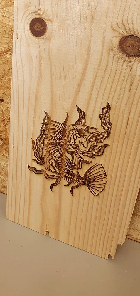 Detaillierte Lasergravur eines Fischskeletts im Tattoo Stil mit Seegras auf Fichtenholz