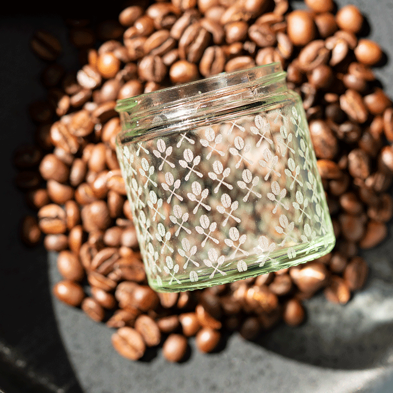 Glasgravur mit Kaffeemuster auf Vorratsglas, umgeben von Kaffeebohnen