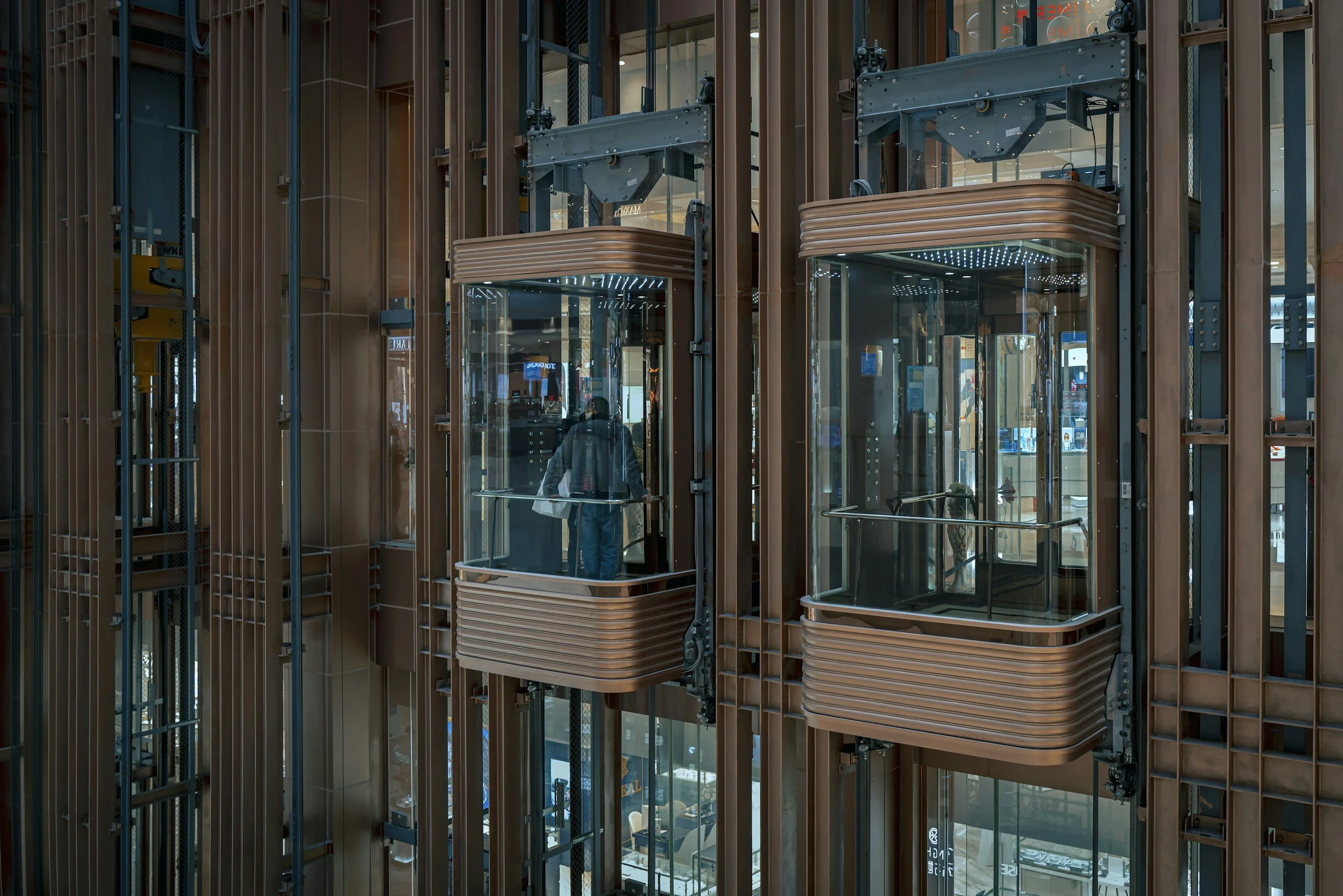 Ein moderner Aufzug im Gebäude mit sichtbarer Innenkabine und Glaswänden, umgeben von einem Holz- oder Metallrahmen.