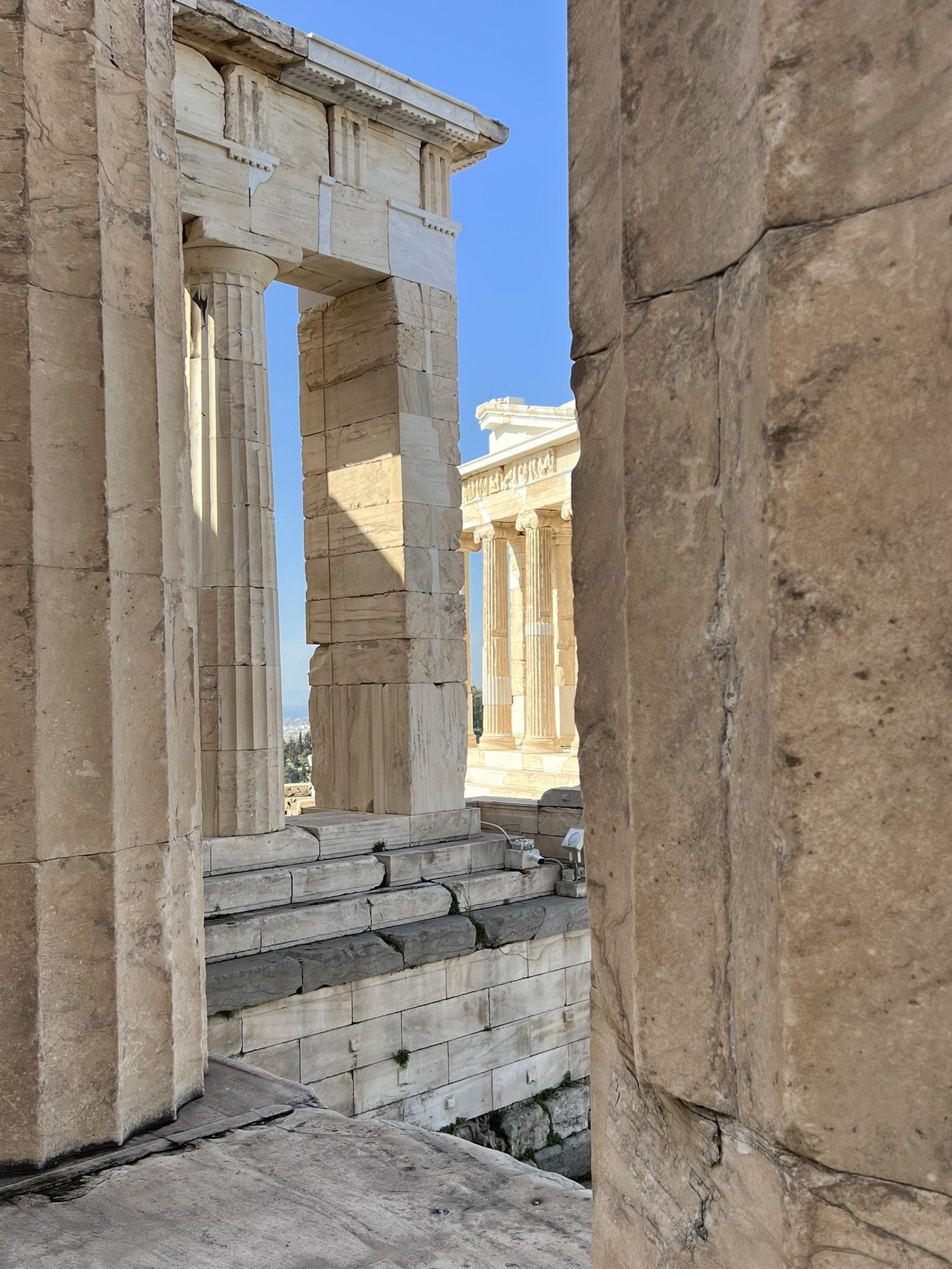Blick durch eine alte, teilweise zerfallene antike Tempelruine aus Marmor mit Säulen gegen einen blauen Himmel.