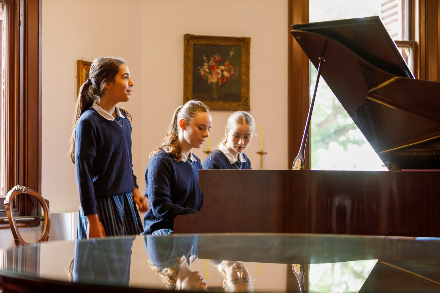 Three young girls in school uniforms are around a grand piano. School and event photography by Jess Grant and Alys Carr, Melbourne Australia
