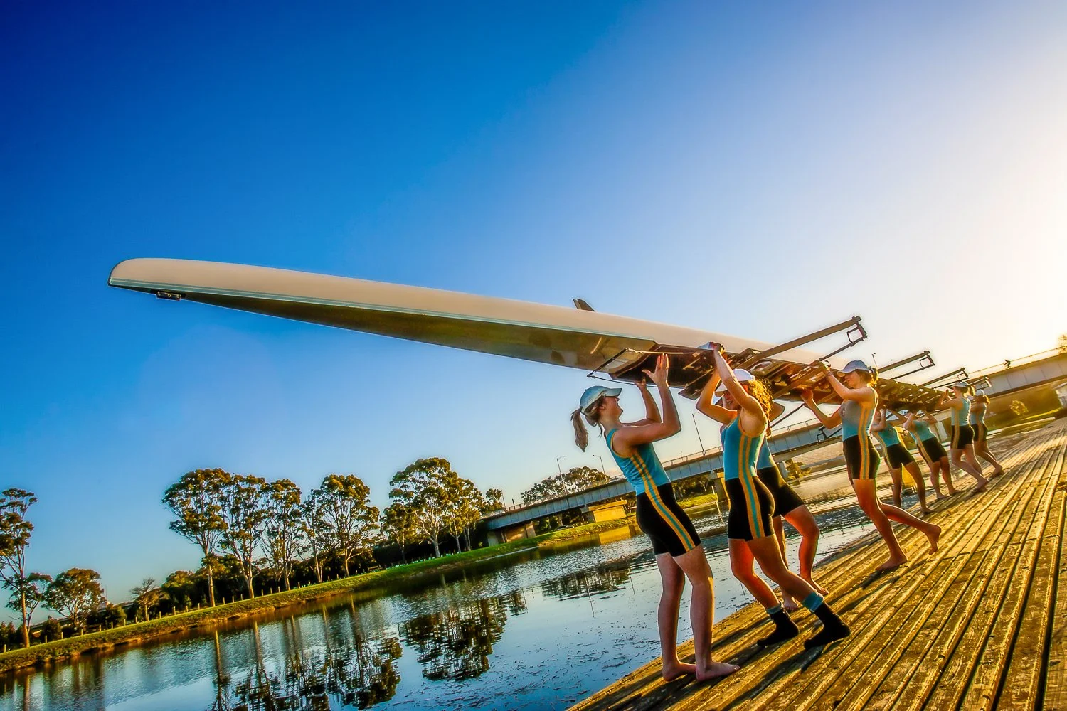 School athletics, rowing photography carrying outrigger canoes on a dock by a river during sunset by Jess Grant and Alys Carr, Melbourne Australia.
