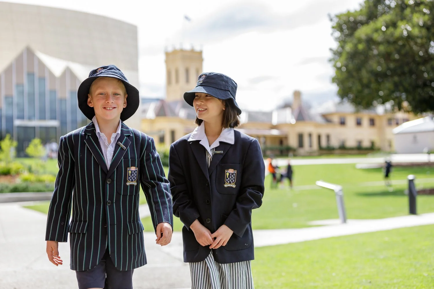 Two school children in navy blue uniforms and hats walking outdoors on a sunny day. School and event photography by Jess Grant and Alys Carr, Melbourne Australia