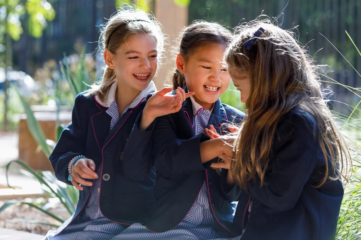 Three girls in school uniforms laughing and playing together outdoors. School photography by Jess Grant and Alys Carr.