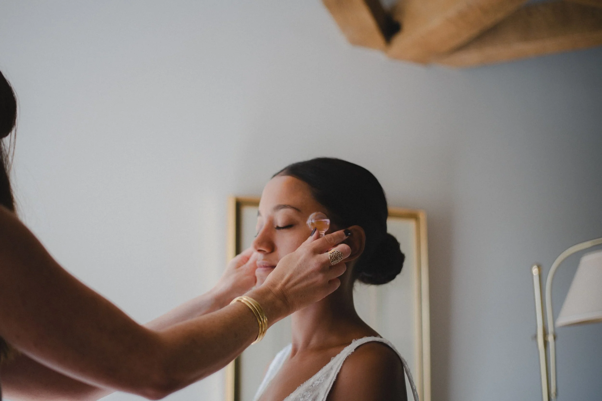 Une femme se fait maquiller ou se fait faire une préparation du visage par une autre personne, dans un cadre intérieur.