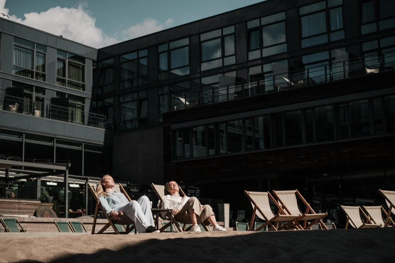 To kvinner sitter i solsenger utenfor et svart hotell