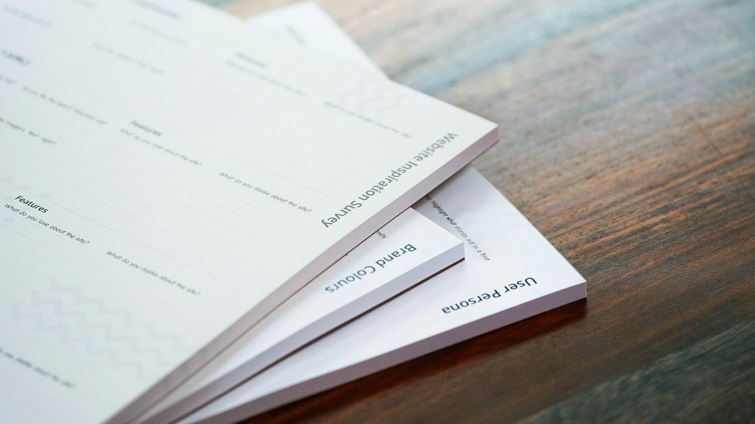 Zwei weiße Feedback-Bögen mit schwarzen Texten auf einem Holztisch, der eine Feedback-Session für einen Branding-Workshop vorbereitet.