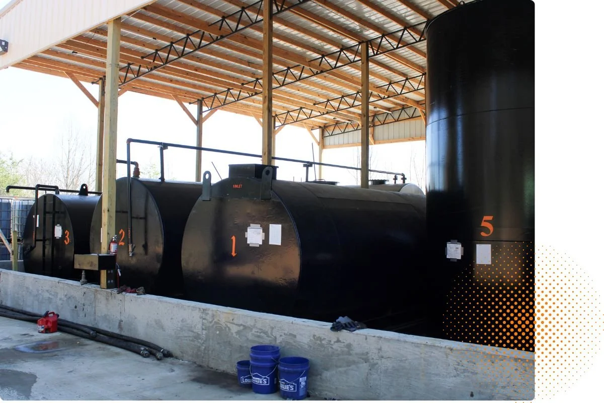 Four large black industrial tanks labeled 1, 2, 3, and 5, stored under a wooden shelter with a metal roof, in an outdoor setting.