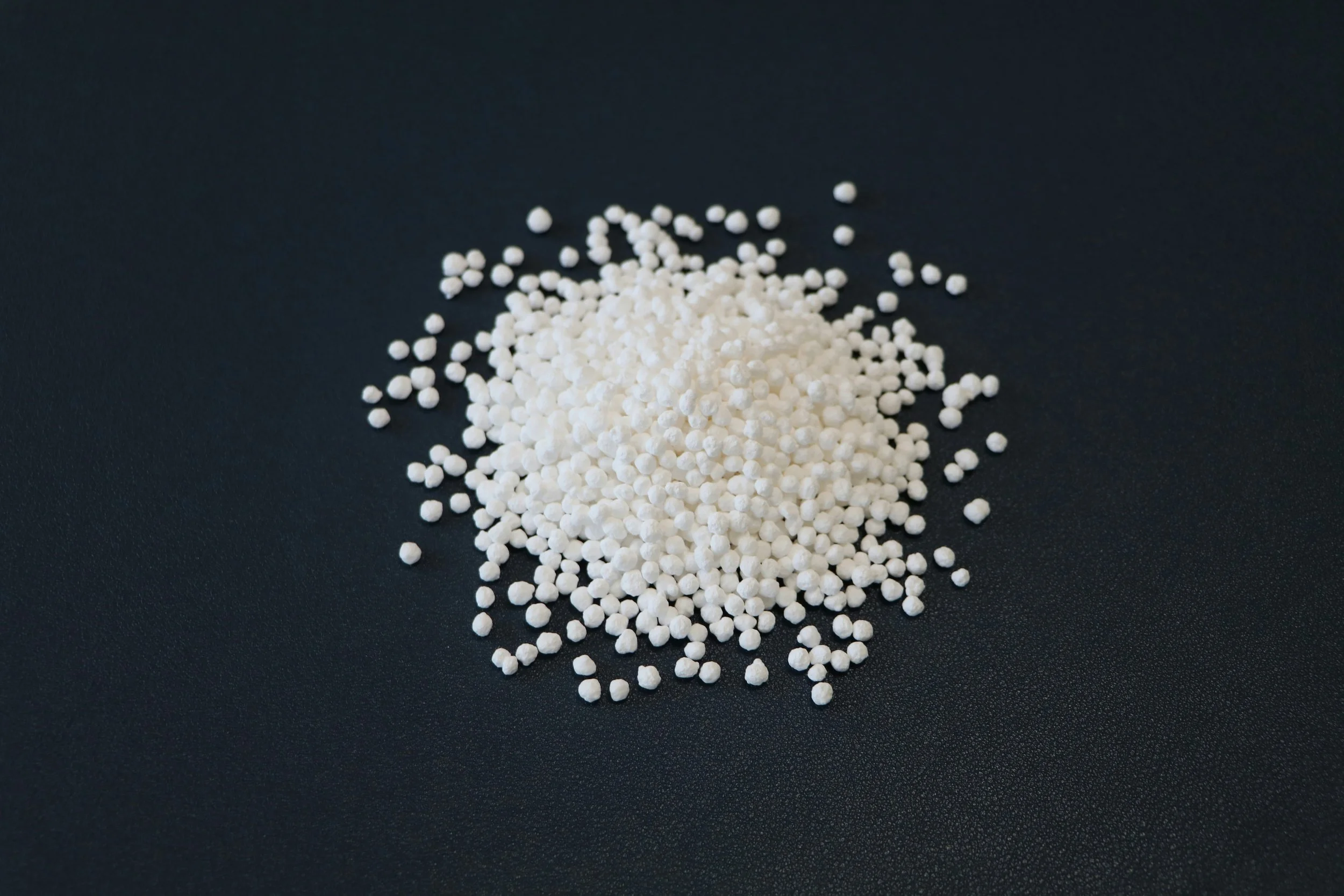 Small white spherical pellets scattered on a dark surface.