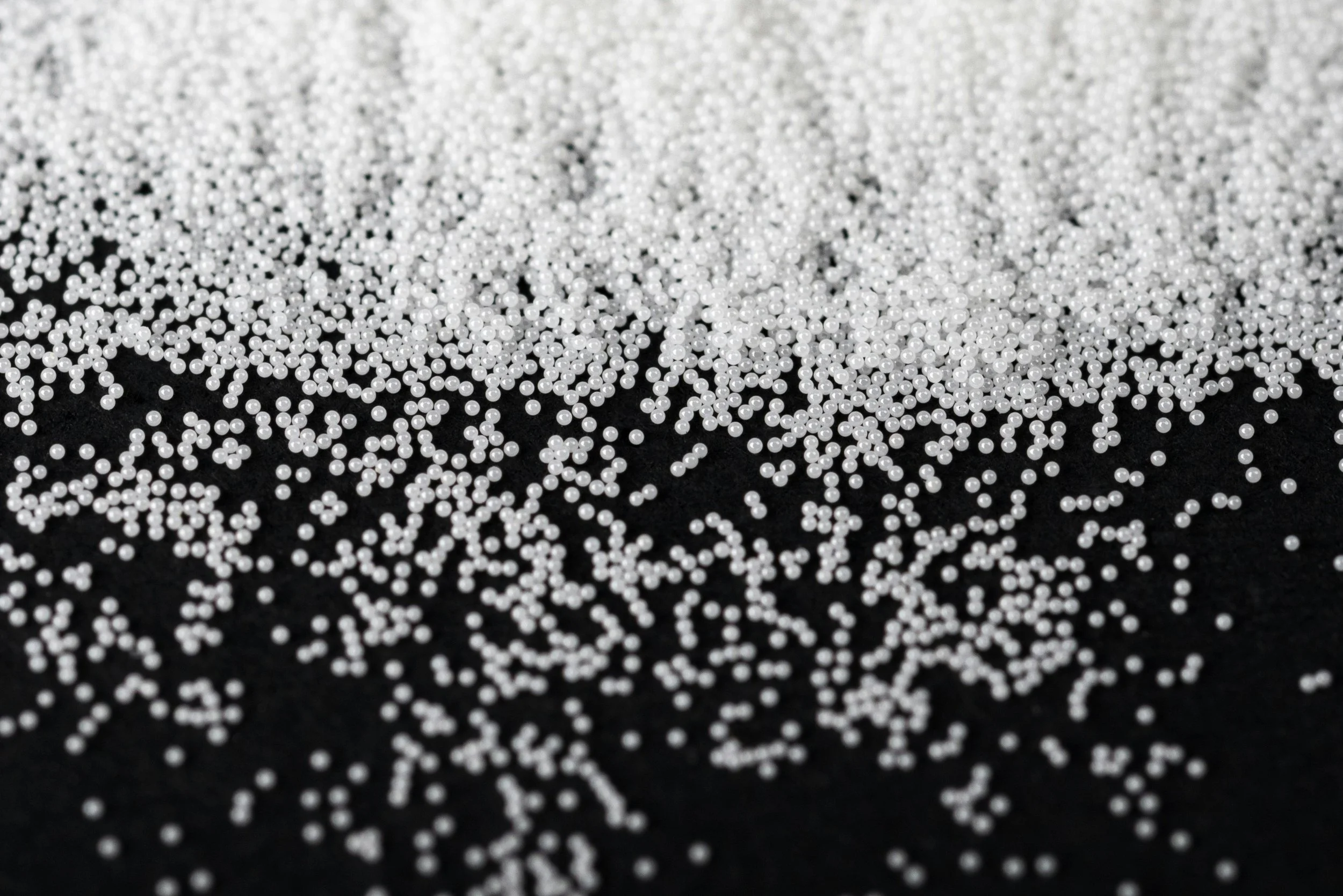 Close-up of small white spherical beads scattered on a black surface.